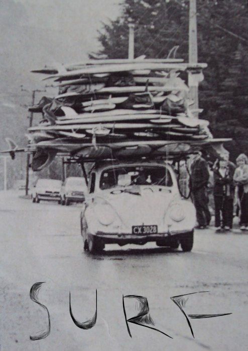 an old car is carrying surfboards on its roof while people stand in the background