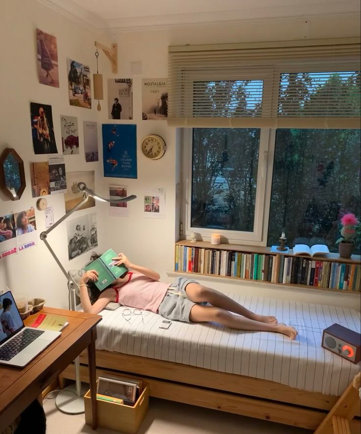 a woman laying on top of a bed next to a desk with a laptop computer