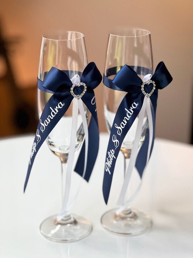 two wine glasses with blue ribbon and name on them sitting next to each other in front of a white table