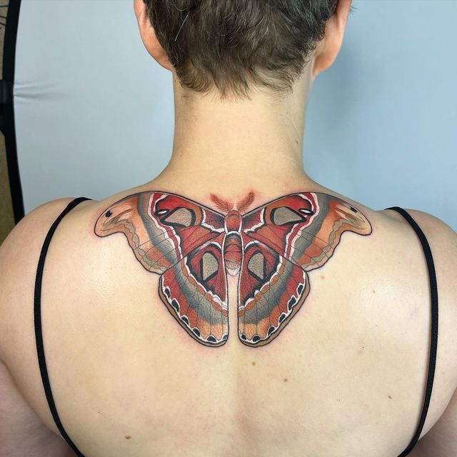 the back of a woman's neck with a colorful butterfly tattoo on her chest