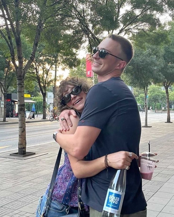 a man and woman hugging each other on the street with trees in the back ground