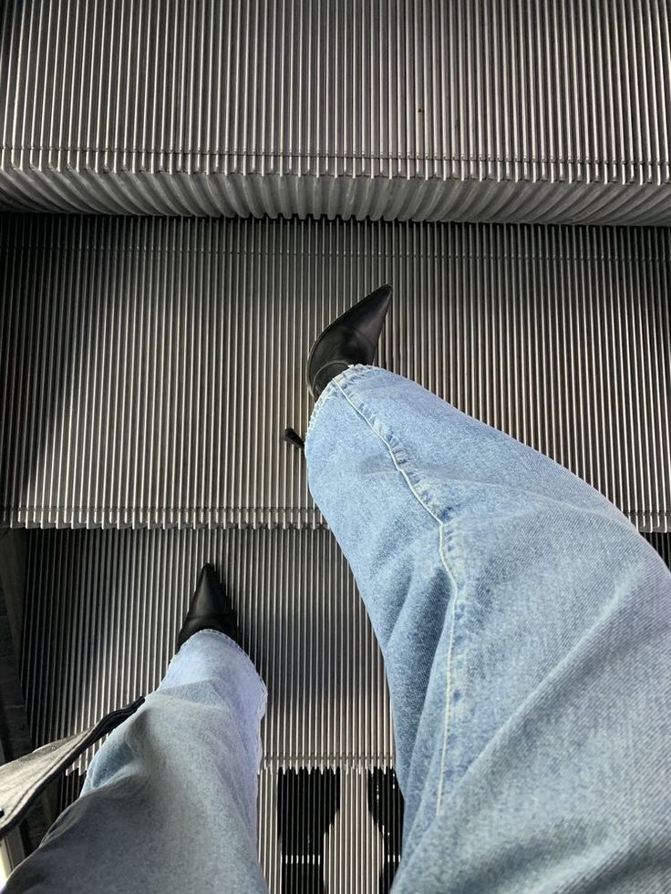 a person standing on an escalator with their feet in the air and wearing blue jeans