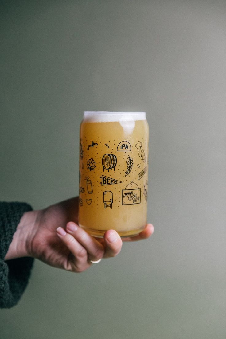 a person holding a beer in their hand with doodles on the lid and bottom