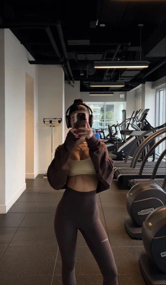 a woman taking a selfie in front of treadmills with her cell phone