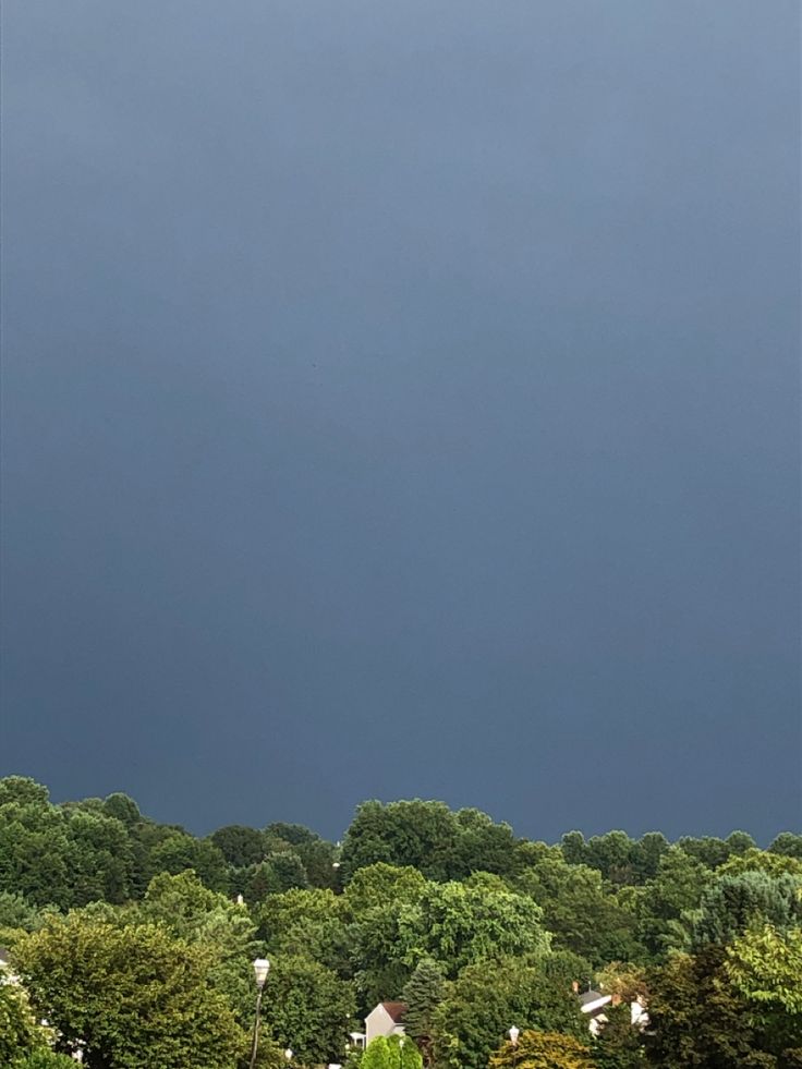 the sky is very dark and cloudy with some trees in the foreground, and houses on the far side