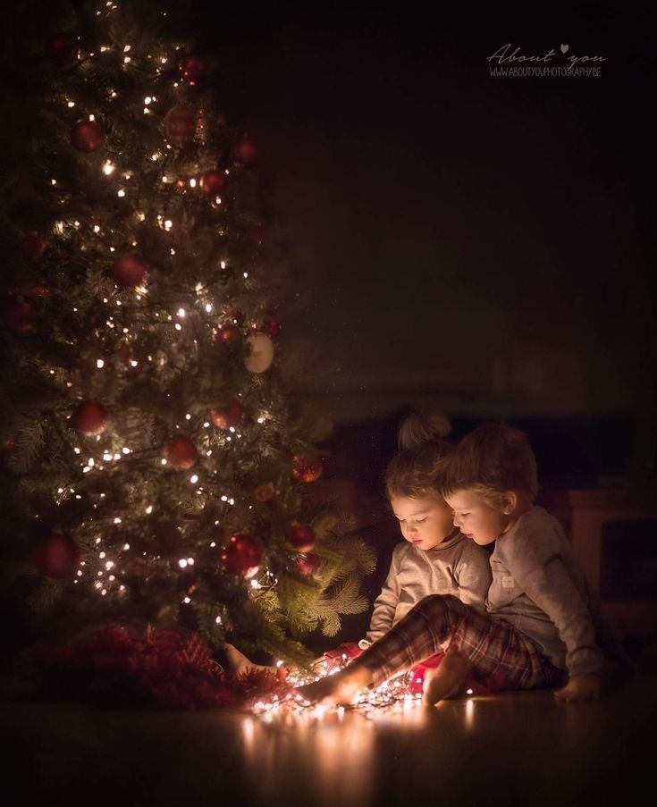 two young children sitting in front of a christmas tree looking at the lights on it