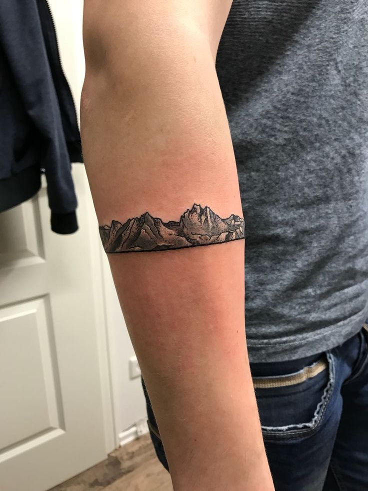 a person with a mountain tattoo on their arm and the mountains behind them are black and white