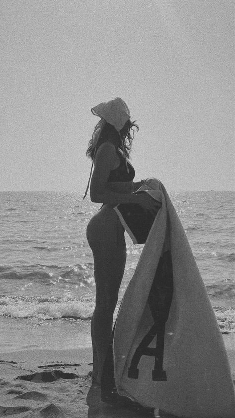 a woman sitting on top of a surfboard next to the ocean in black and white