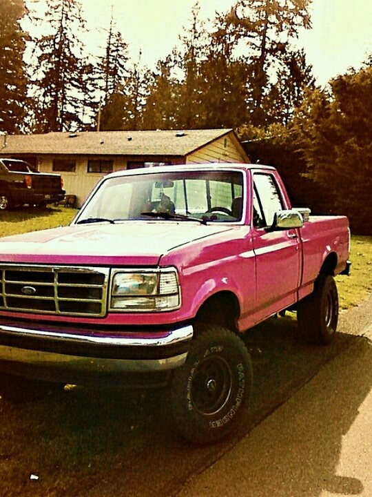 a pink pick up truck parked on the side of a road in front of a house