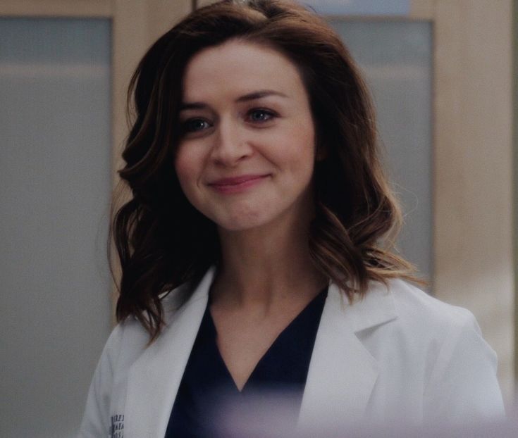 a woman in a white lab coat smiles at the camera while looking off into the distance