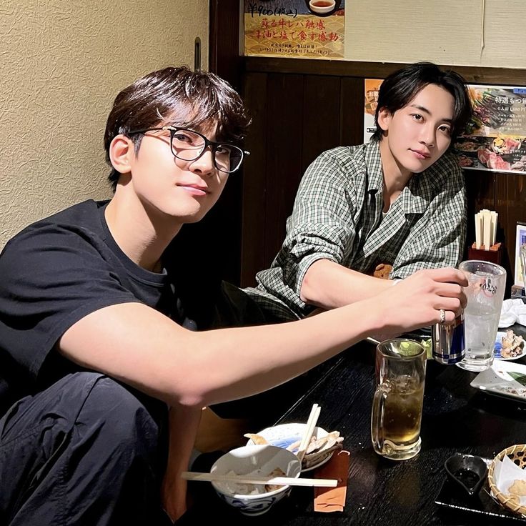 two young men sitting at a table with food and drinks in front of them,