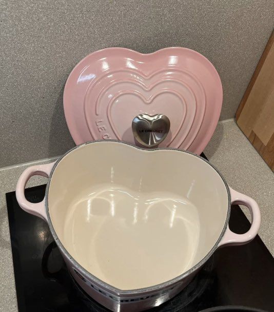 a heart shaped pot on top of a stove next to a pink oven mitt