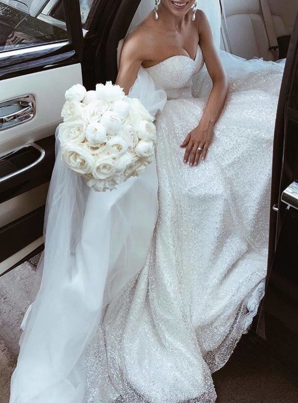 a bride sitting in the back of a car with her bouquet on her lap and smiling