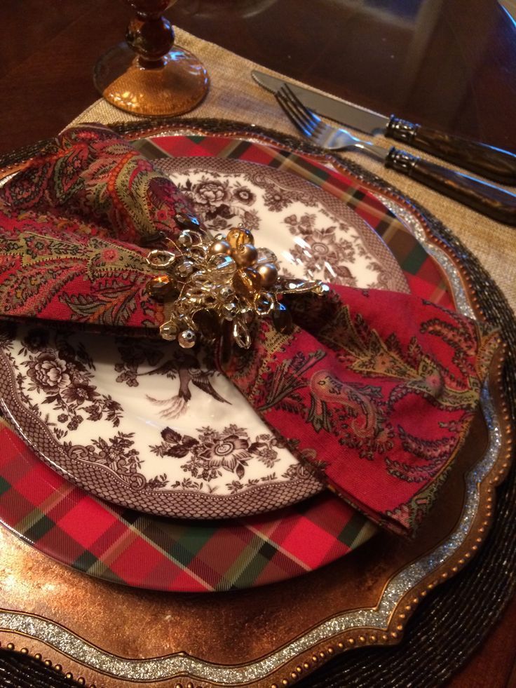 a place setting with red and green plaid napkins, silverware and a gold plate