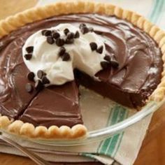 a chocolate pie with whipped cream and chocolate chips on top sits in a glass dish