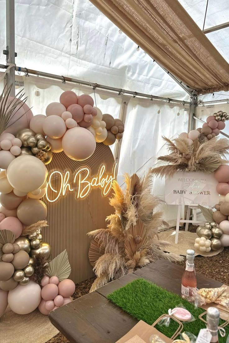 a table topped with lots of balloons next to a white tent covered in grass and palm trees