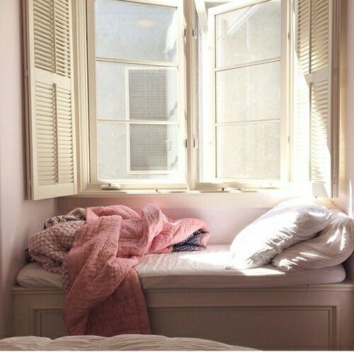 an unmade bed sitting in front of a window with two pillows on top of it