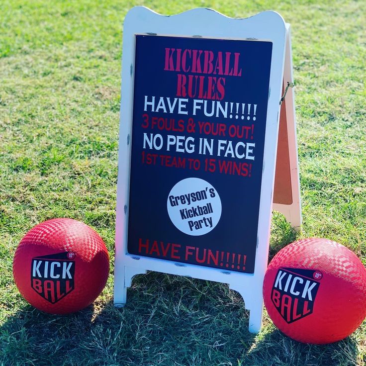 two red balls sitting in the grass next to a sign that says kickball rules have fun