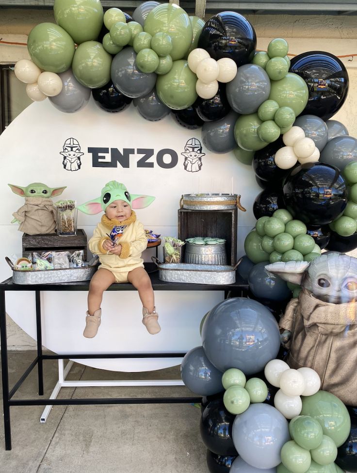 a baby yoda sitting on top of a table surrounded by balloons and star wars decorations