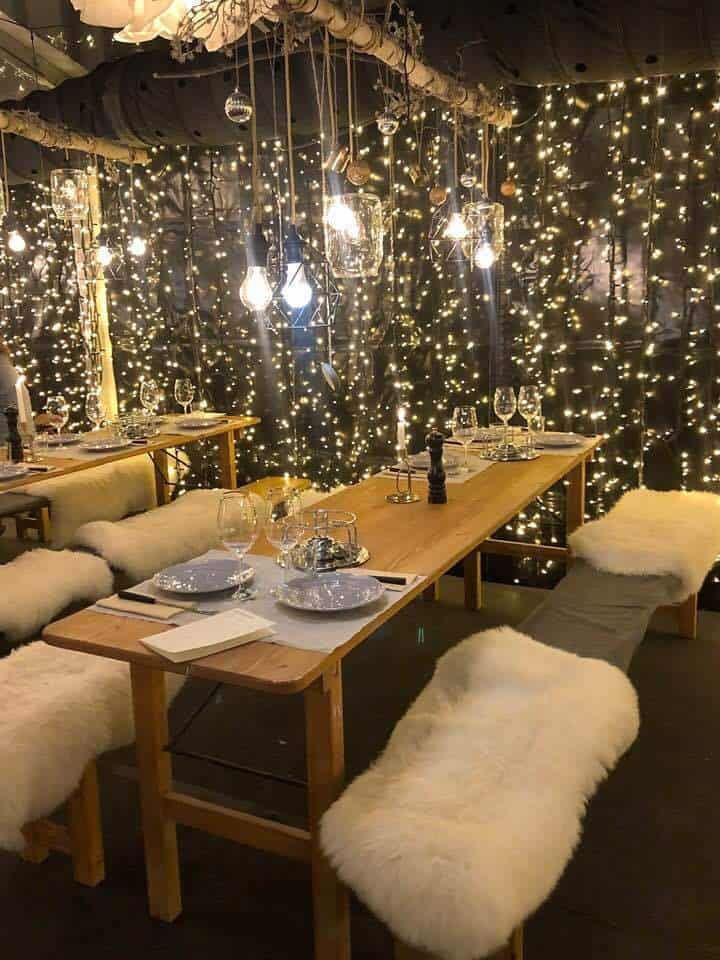 a dining room with lights on the wall and white sheepskin chairs at the table