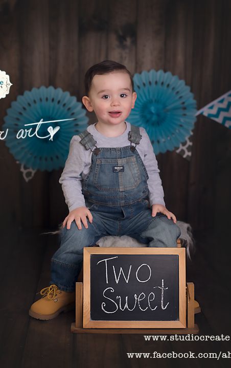 a little boy sitting in front of a chalkboard with the words two sweet written on it