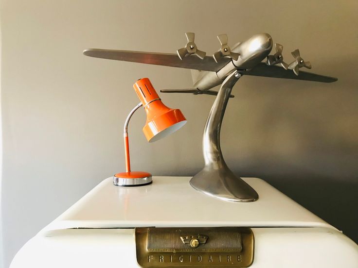 an orange lamp sitting on top of a white table next to a metal airplane sculpture