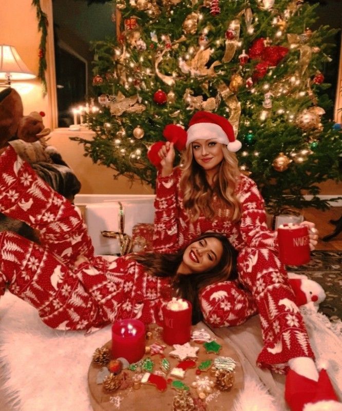 two women in christmas pajamas sitting on the floor next to a christmas tree with candles