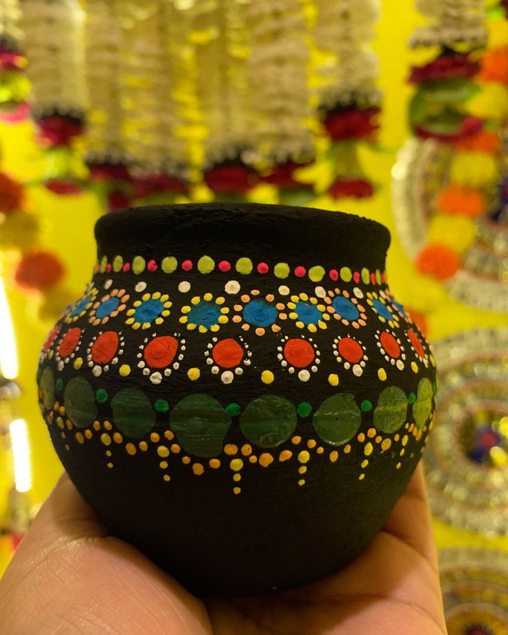 a hand holding a black vase with colorful designs on it