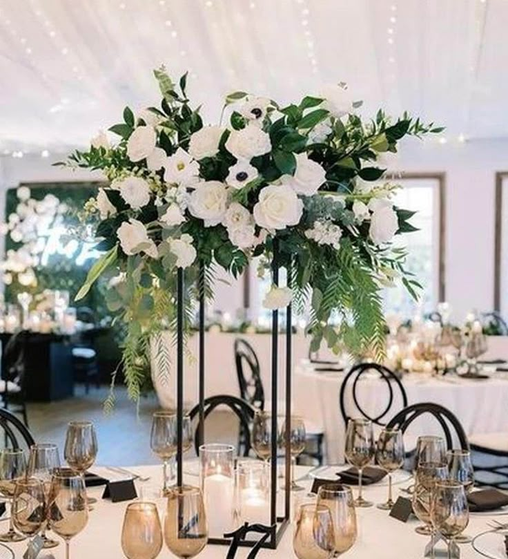 an elegant centerpiece with white flowers and greenery sits on a table at a wedding reception