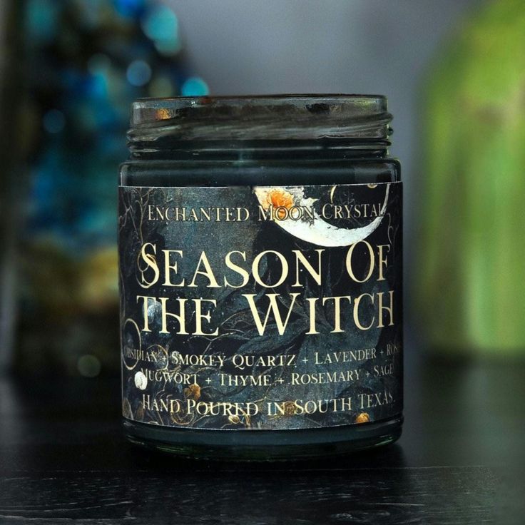 a jar of season of the witch candle sits on a table next to a potted plant