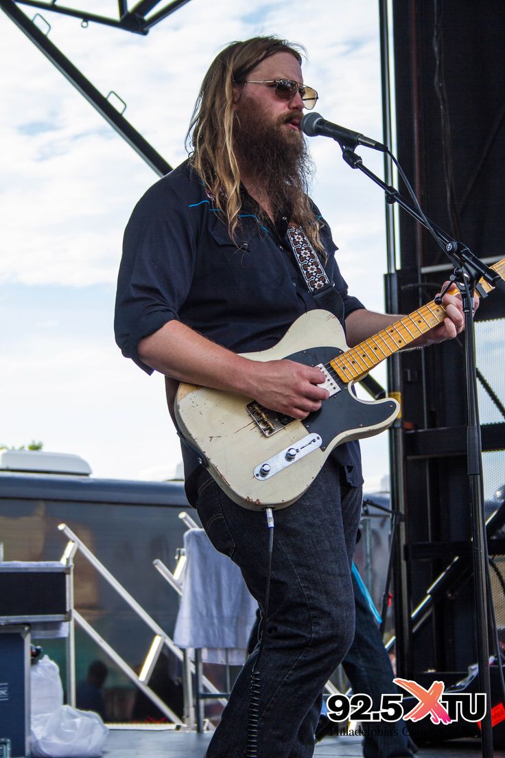 a man with long hair and beard playing an electric guitar on stage at a music festival