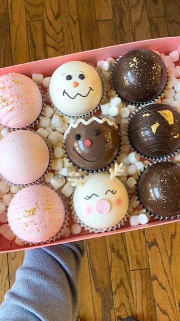 a person holding a pink box filled with chocolate covered donuts and marshmallows