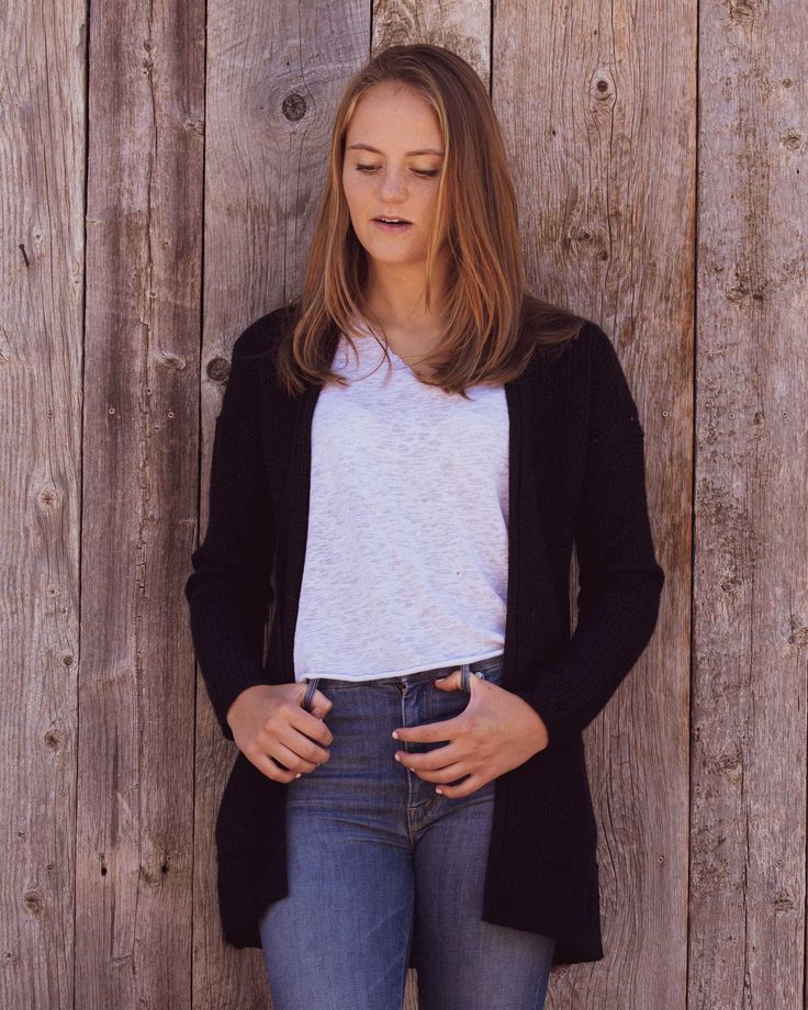 a woman leaning against a wooden fence with her hands in her pockets and looking down