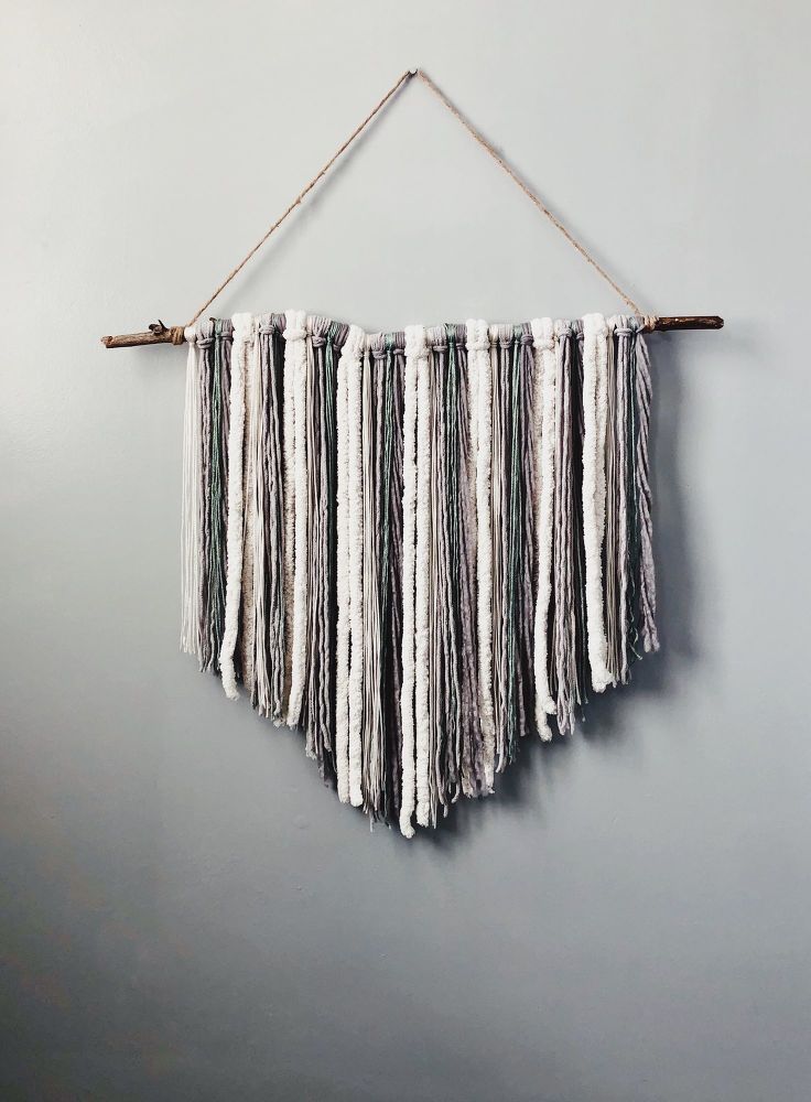 the wall hanging is made out of white yarn and has several different fringes on it