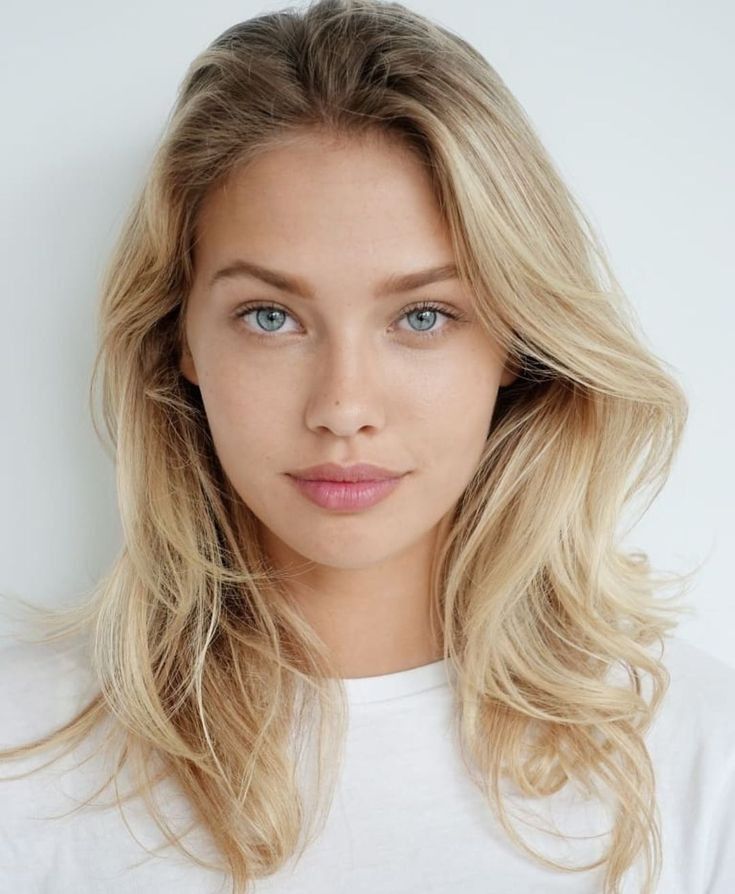 a woman with long blonde hair and blue eyes wearing a white t - shirt looking at the camera