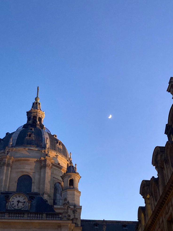 an old building with a clock on it's face and the moon in the sky