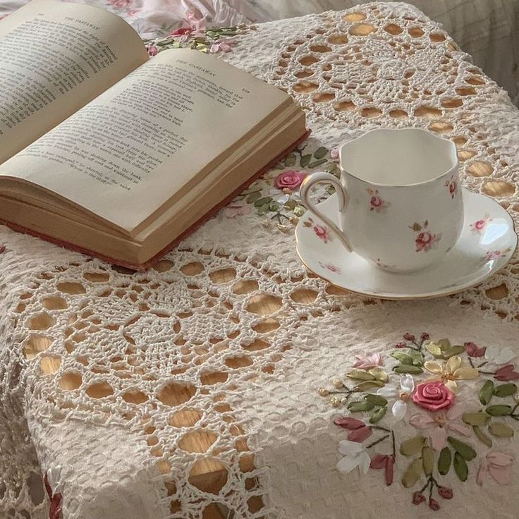 an open book on a doily with a cup and saucer next to it