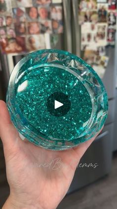 a person holding up a glass bowl with green glitter on it in front of a refrigerator