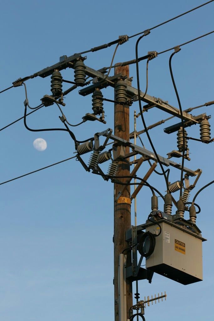 an electric pole with power lines and telephone poles on it, against a blue sky