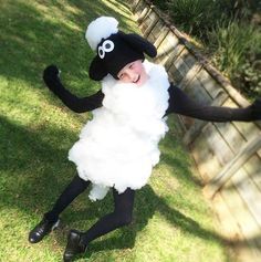 a child dressed up as a sheep in the grass with his arms out and legs spread wide