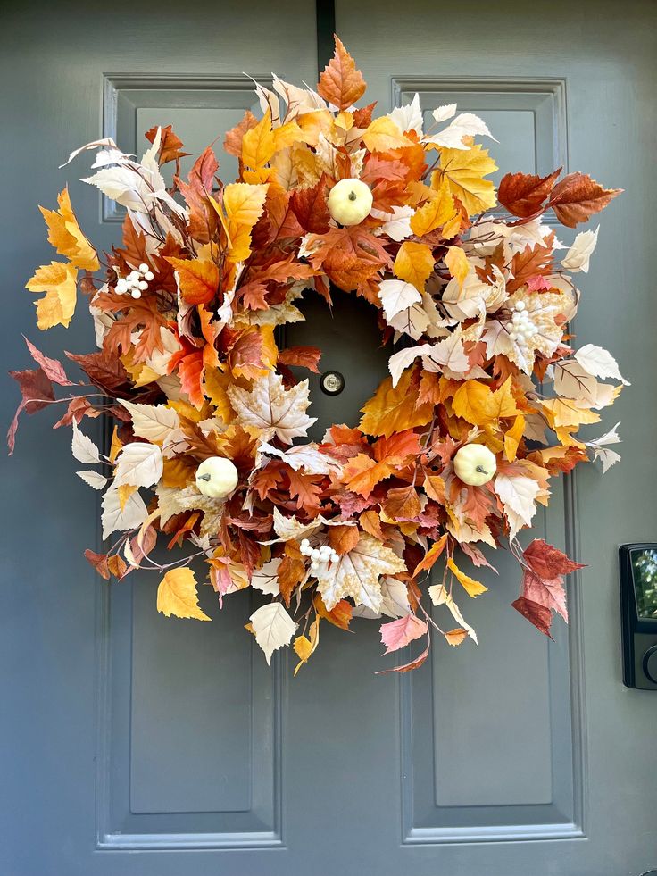 a wreath is hanging on the front door with apples and autumn leaves around it,