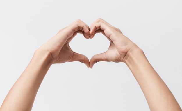 two hands making a heart shape with their fingers against a white background in front of the camera