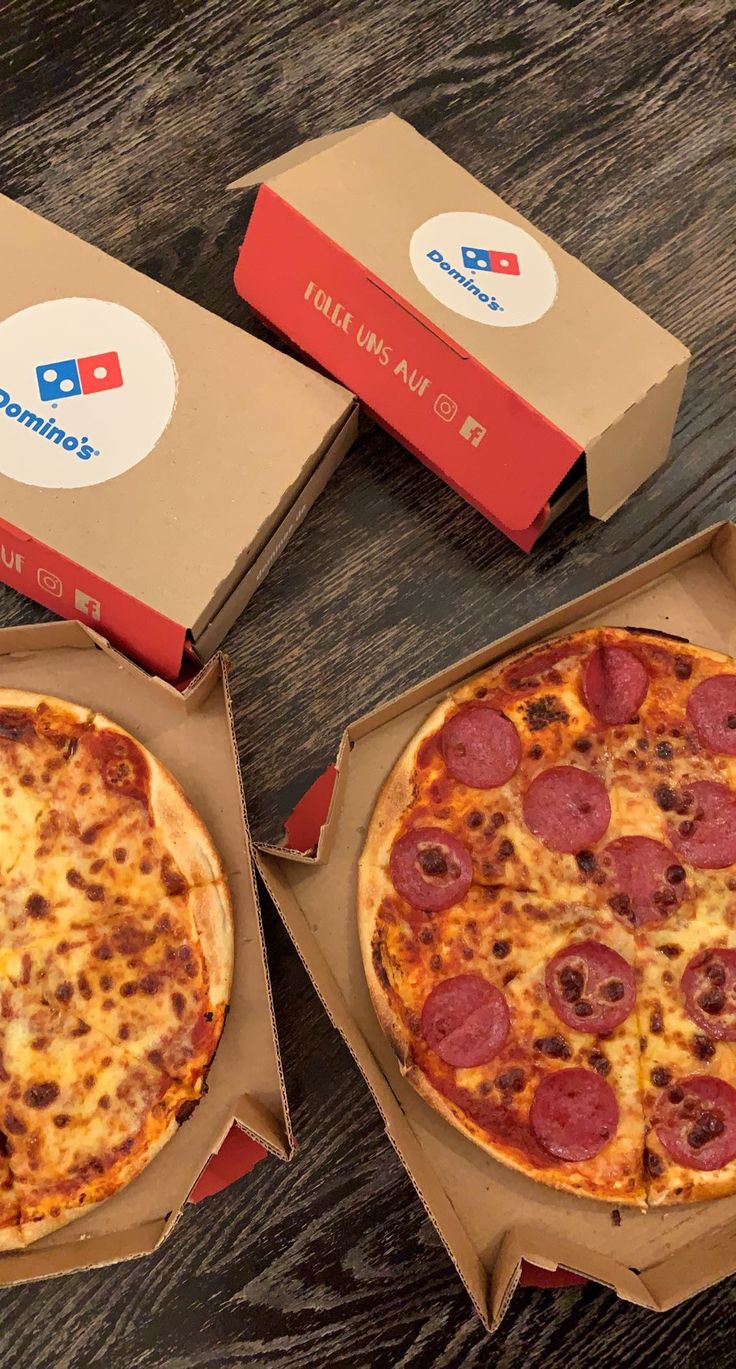 two pizzas in boxes sitting on a table