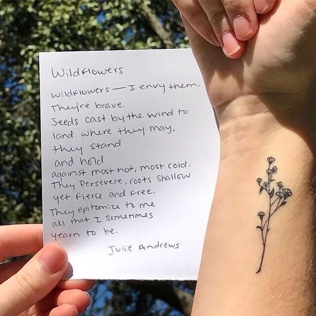 someone holding up a piece of paper with a flower tattoo on their left arm that says wildflowers