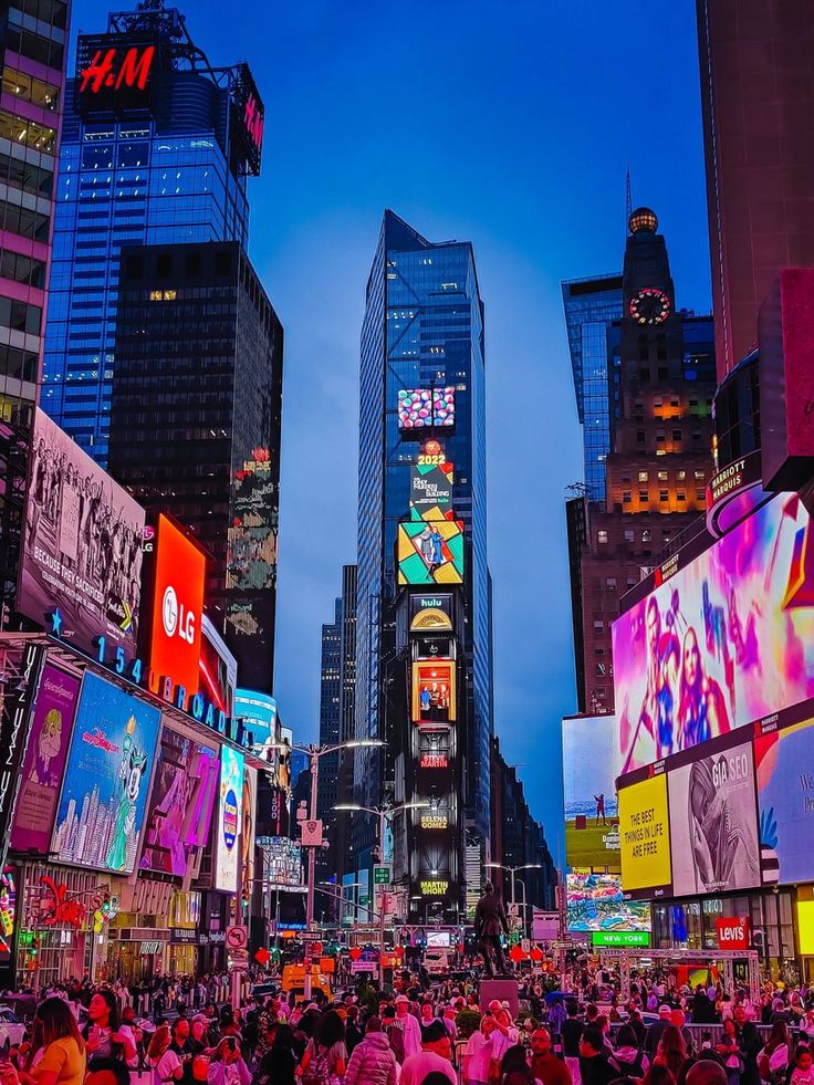 a crowded city street filled with lots of people and tall buildings at night time, all lit up