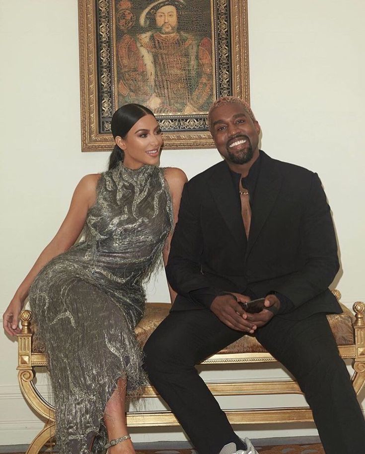 a man and woman sitting on a wooden bench in front of a wall with paintings