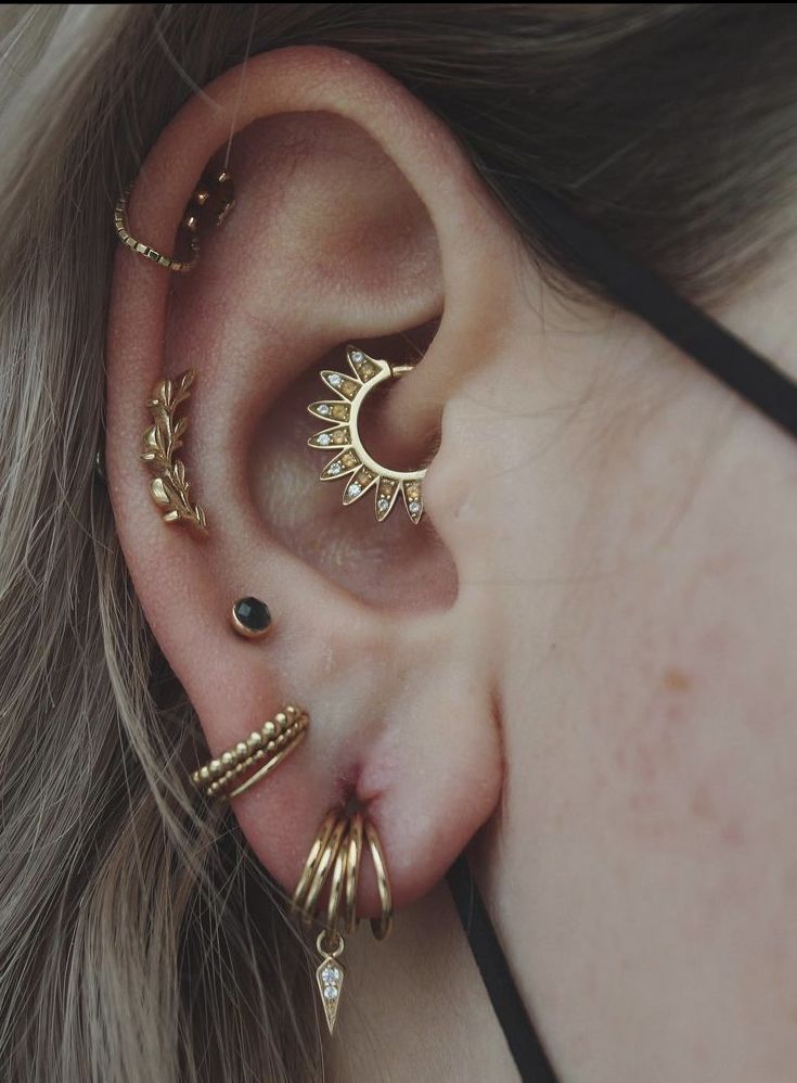 a close up of a person wearing ear piercings with gold colored metal spikes and black stones