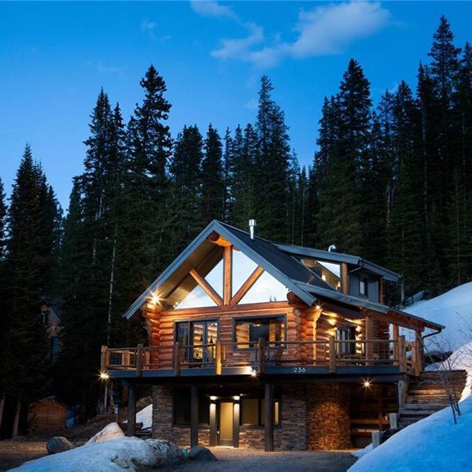 a log cabin in the woods lit up at night with lights shining on it's windows