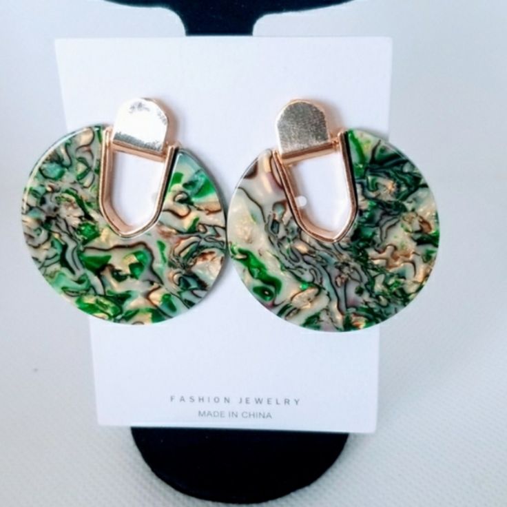 a pair of green and gold earrings on top of a white card with a black holder