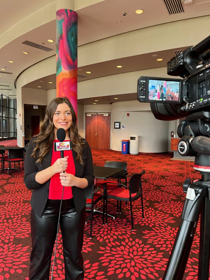 a woman standing in front of a camera holding a microphone